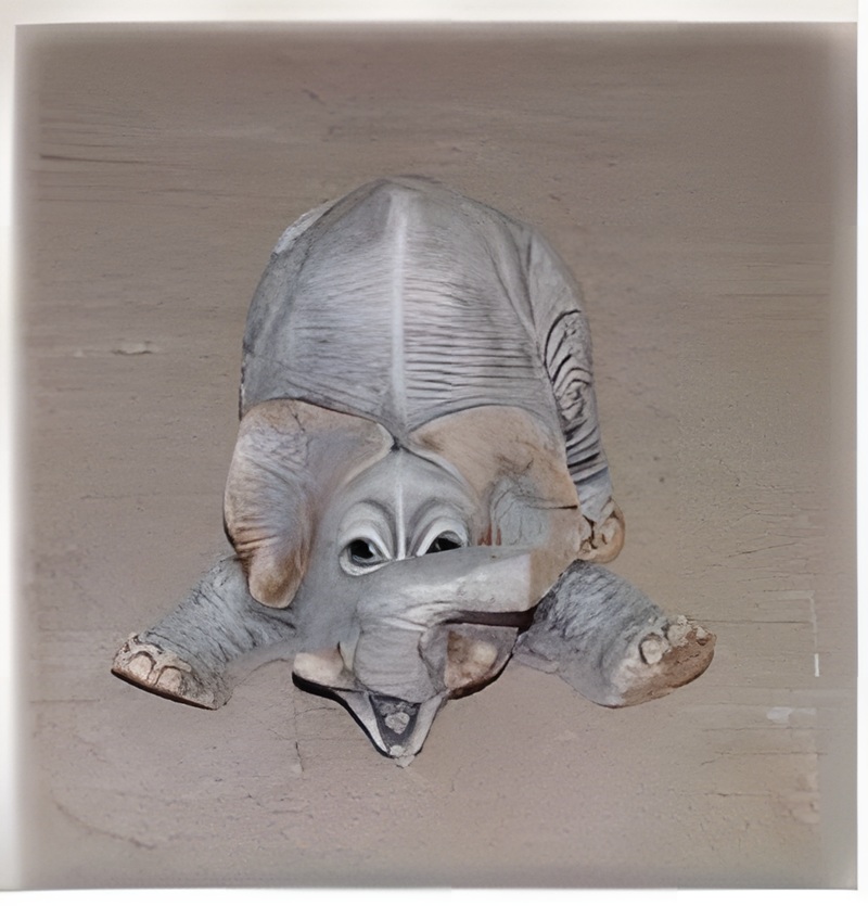 09040100354 Figura decorativa de una elefantita tumbada boca abajo fabricada en piedra artificial con acabados realistas.