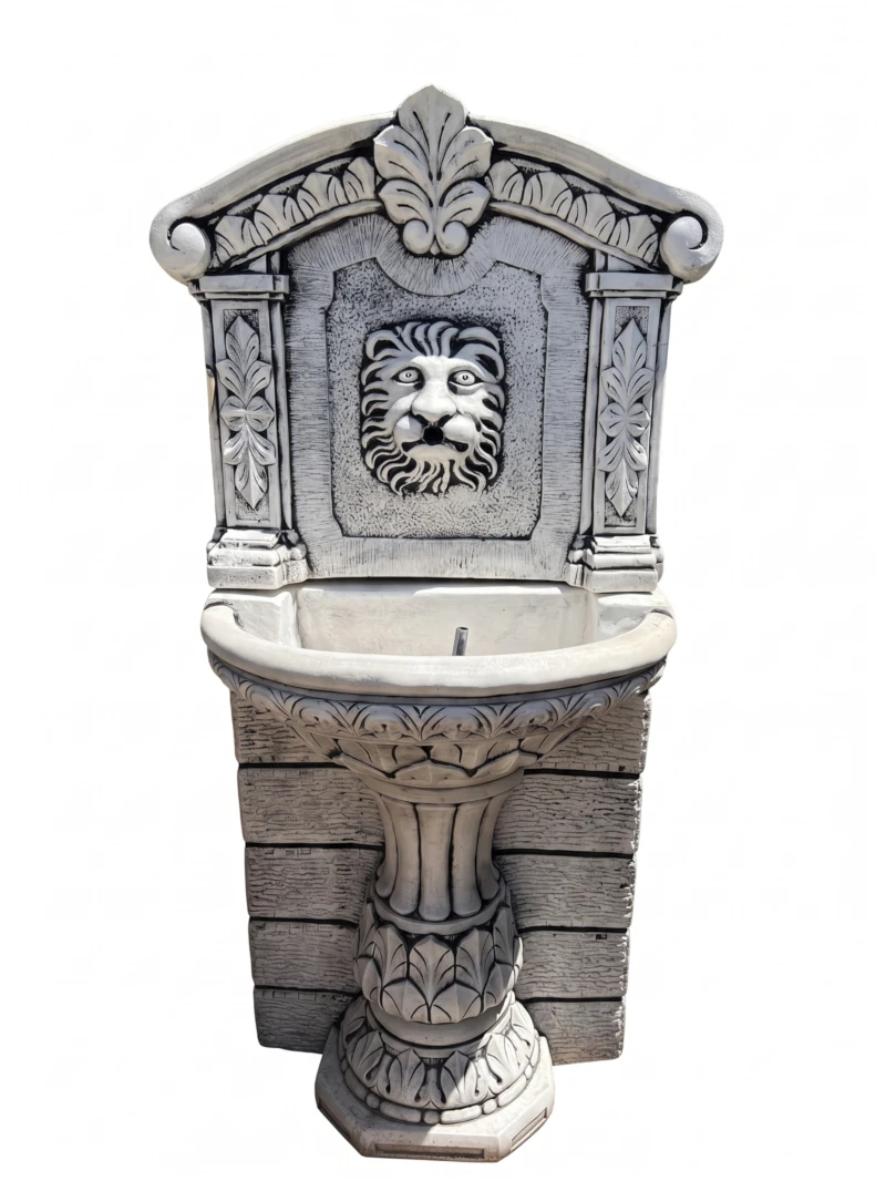 10010100623 Fuente de pared clásica de piedra artificial con relieve de cabeza de león, copete ornamentado y columna estriada para instalación en muros de jardín.